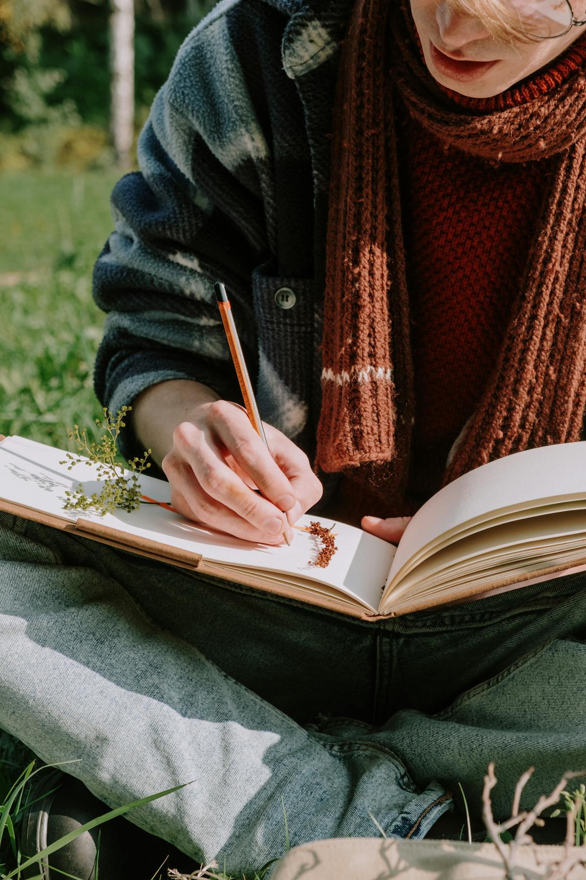 Personne assise dans l’herbe, écrivant dans un carnet nature avec spécimens végétaux